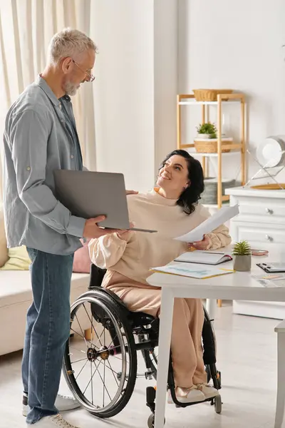 Eine behinderte Frau im Rollstuhl und ihr Mann arbeiten zu Hause an einem Laptop in der Küche. — Stockfoto
