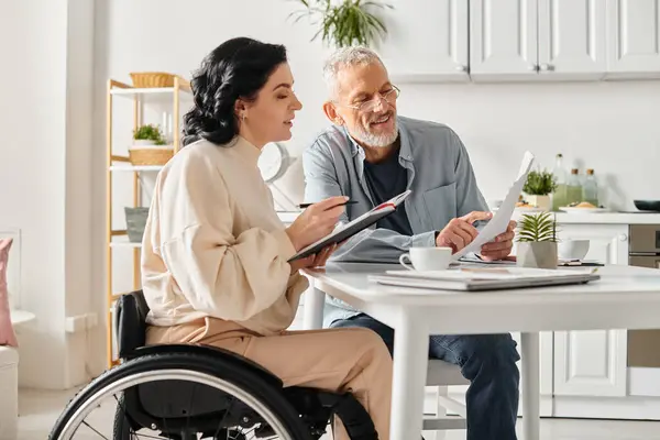Un hombre y una mujer en sillas de ruedas comparten ideas sobre el presupuesto familiar en un acogedor entorno de cocina. - foto de stock