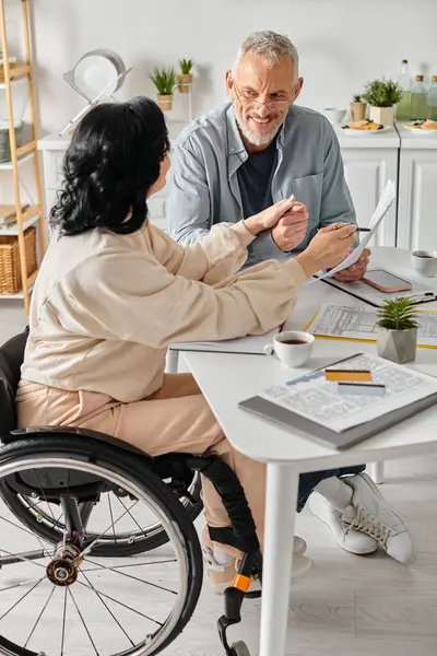 A disabled woman in a wheelchair and her caring husband planning family budget together - foto de stock