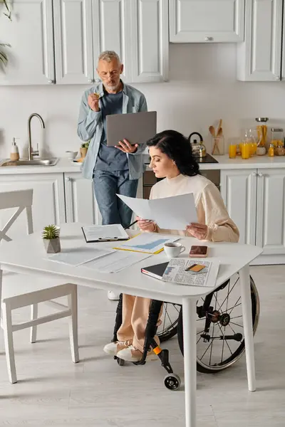 Eine behinderte Frau im Rollstuhl sitzt mit ihrem Mann an einem Küchentisch. — Stockfoto