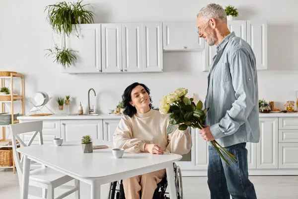 A man tenderly stands beside his wife in a wheelchair, sharing a moment of connection and support in their kitchen at home. — Photo de stock