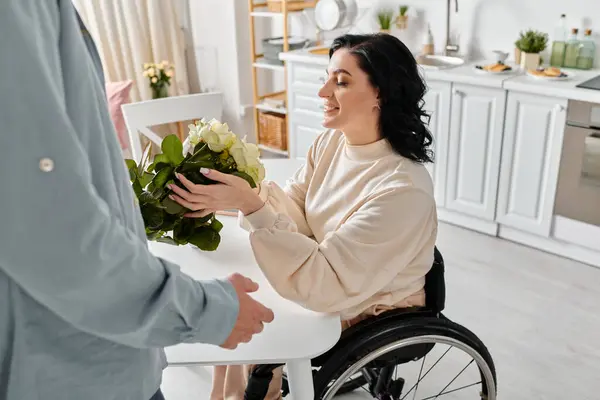 A disabled woman in a wheelchair holding a vibrant bouquet of flowers, surrounded by love in her home kitchen. — Photo de stock