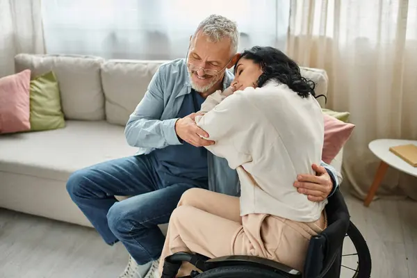 A disabled woman in a wheelchair embracing her husband with love and affection in a cozy living room setting. — Stock Photo