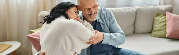 A disabled woman in a wheelchair sits next to her husband on a cozy couch in their living room. — Stock Photo