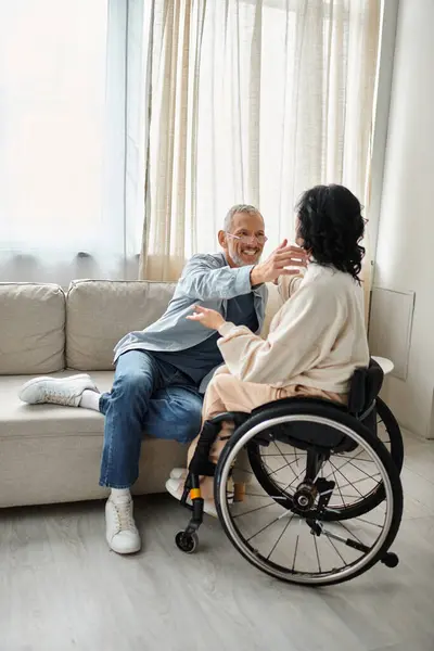 A man and a disabled woman hugging each other affectionately in a cozy living room. - foto de stock