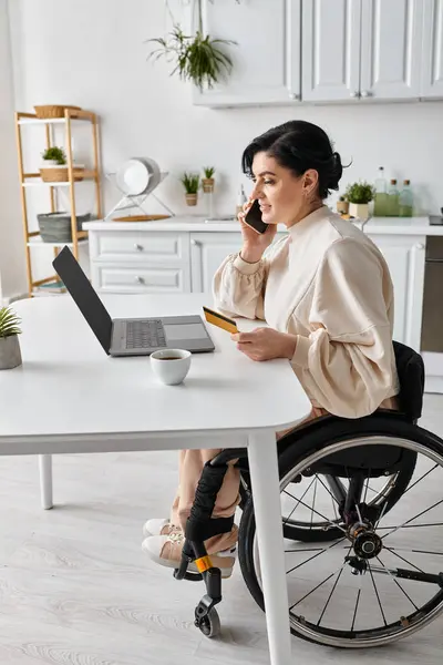 A disabled woman in a wheelchair working remotely from her kitchen, talking on a cell phone. - foto de stock