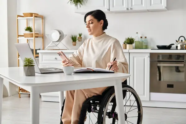 Una donna disabile in sedia a rotelle lavora sul suo portatile a casa in cucina, mostrando produttività e indipendenza. — Foto stock