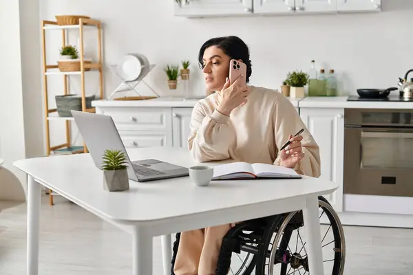 Mujer en silla de ruedas trabajando a distancia, charlando en el teléfono celular en la cocina. - foto de stock