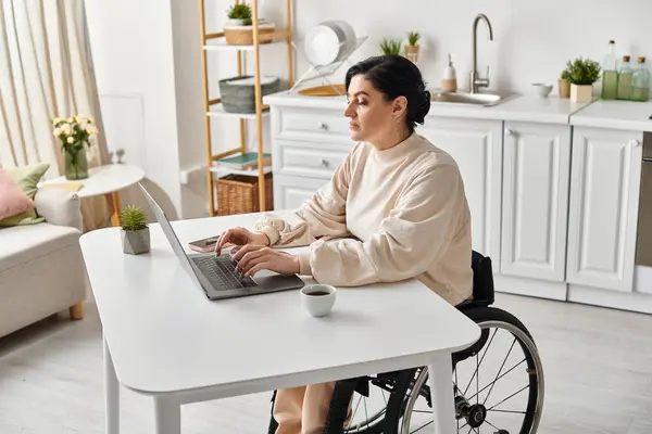 Uma mulher deficiente em uma cadeira de rodas trabalha remotamente em seu laptop na cozinha, mostrando a independência digital. — Fotografia de Stock