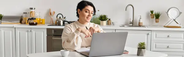 Donna si siede al suo tavolo da cucina, focalizzata sul suo schermo del computer portatile mentre lavora in remoto. — Foto stock