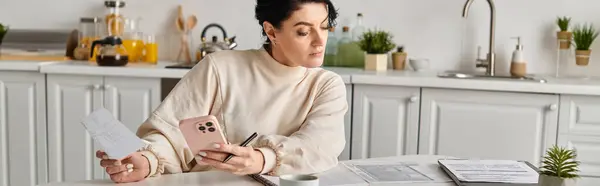 Frau benutzt Handy, während sie von ihrem Küchentisch aus arbeitet. — Stockfoto