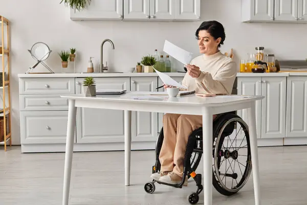Eine Frau im Rollstuhl sitzt in ihrer Küche und hält gedankenverloren einen Zettel in der Hand, der sich auf ihre kreative Arbeit konzentriert. — Stockfoto