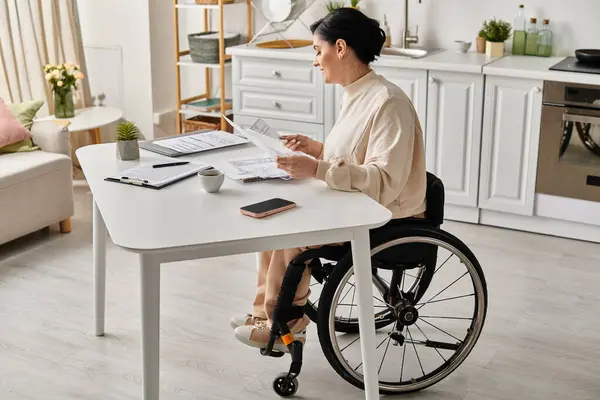 A disabled woman in a wheelchair engaging in remote work at a kitchen table. — Stock Photo