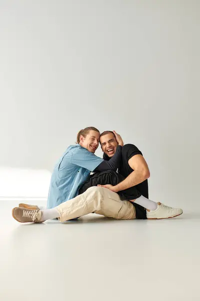 Dos hombres, una atractiva y cariñosa pareja gay, sentados con gracia en un piso blanco. - foto de stock