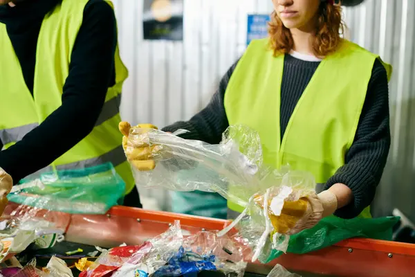 Young volunteers in gloves and safety vests are sorting trash together in a bin. - foto de stock