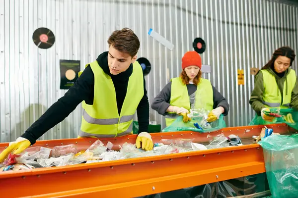 Young volunteers in gloves and safety vests sort trash on a conveyor belt, promoting eco-consciousness. - foto de stock