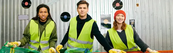 Three young volunteers in safety vests and gloves proudly holding bananas while sorting trash together. — Stock Photo