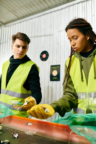Young volunteers in gloves and safety vests standing in front of a table sorting trash together. — Stock Photo