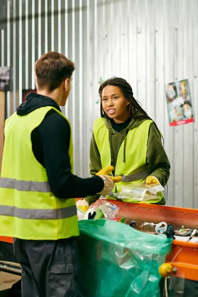 A man and a woman, in gloves and safety vests, standing in front of a table sorting trash as eco-conscious individuals. — Fotografia de Stock