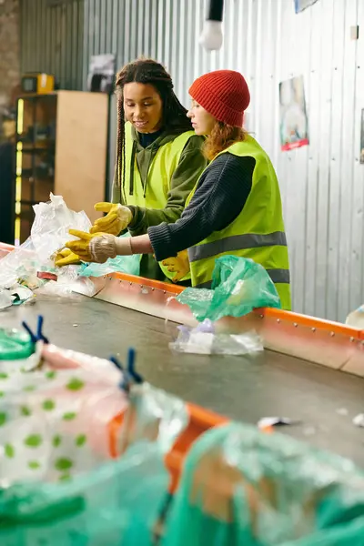 Two young volunteers in gloves and safety vests sorting trash, standing together. — стокове фото