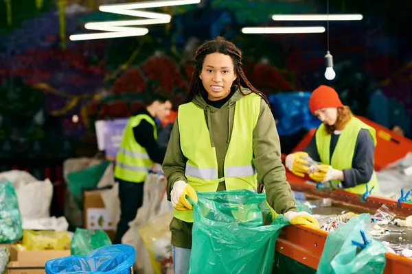 Young volunteer in yellow vest sorts trash, holding green bag at eco-conscious event. — Stock Photo