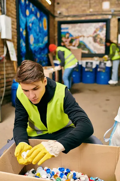 A young man in a bright yellow safety vest and gloves sorts trash with fellow eco-conscious volunteers. - foto de stock