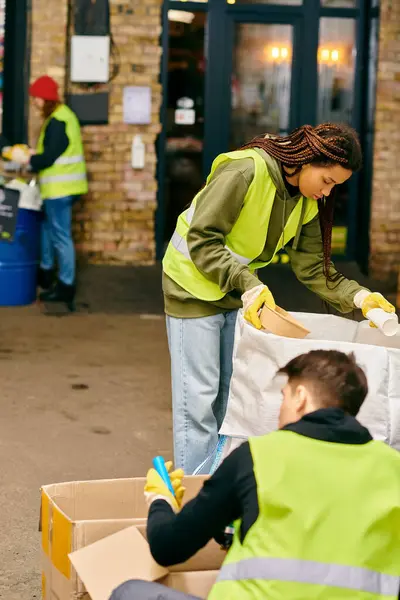 A woman in a yellow vest and a man in a green vest, eco-conscious, sorting trash together as young volunteers. — стоковое фото