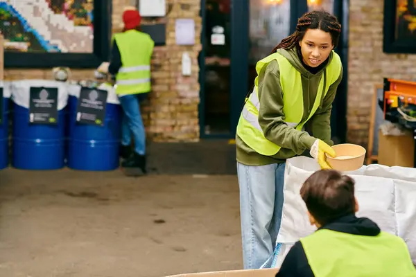 A woman wearing a vibrant yellow jacket, participating in recycling by holding a bowl. - foto de stock
