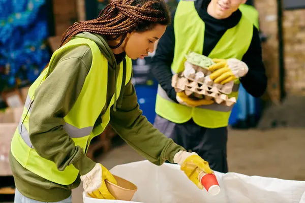 Young volunteers in green and yellow vest sorting trash, embodying eco-conscious efforts together. — Stock Photo