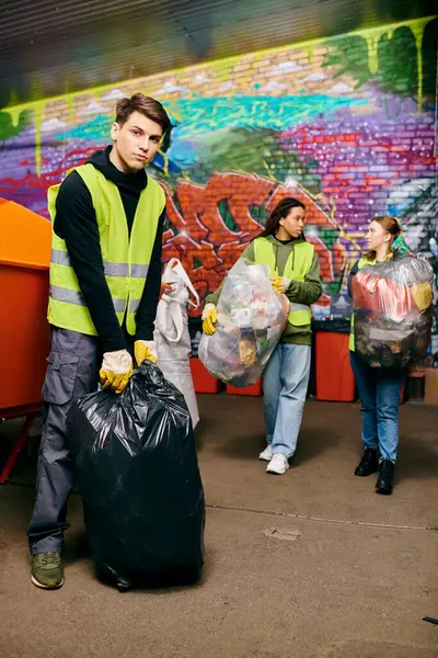 Young volunteers in gloves and safety vests sorting trash in front of a wall, taking action for a cleaner environment. — Fotografia de Stock