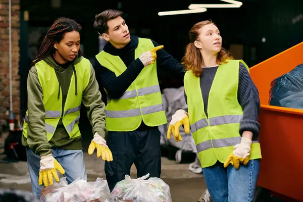Group of young volunteers in gloves and safety vests sorting through a pile of garbage together. — стокове фото