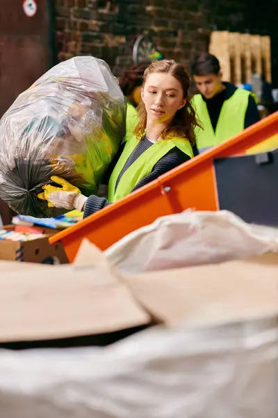 Young eco-conscious volunteers in gloves and safety vests sorting trash together around a pile of boxes. — Stock Photo