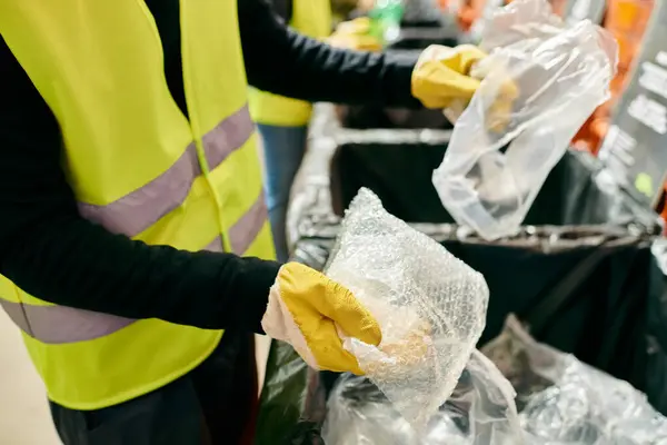 A person in a yellow vest and yellow gloves joins young volunteers in sorting trash as part of an eco-conscious effort. - foto de stock