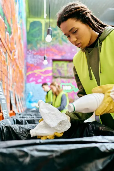 A young volunteer in gloves sorts trash with other eco-conscious people in safety vests. — Fotografia de Stock