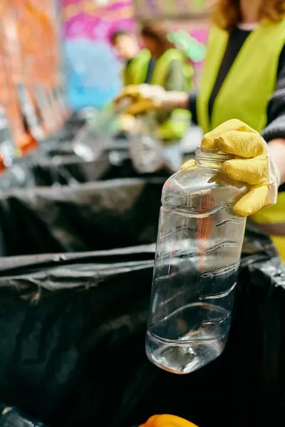 A young volunteer in gloves and a safety vest holds a plastic bottle, promoting eco-conscious actions. — Stock Photo