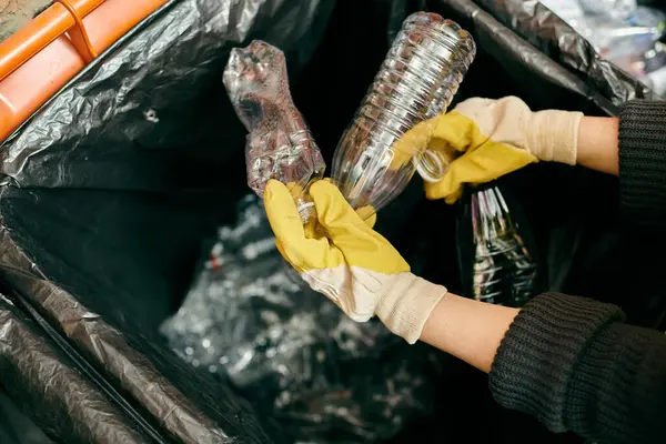 A person in bright yellow gloves meticulously cleaning and sorting trash — стоковое фото