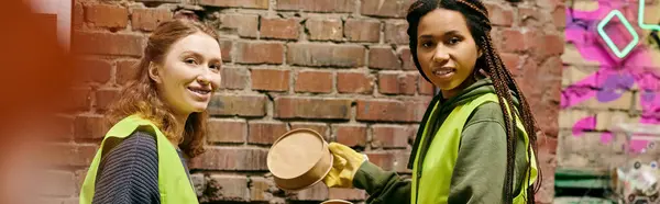 Two young volunteers in safety vests and gloves sorting trash next to a brick wall, demonstrating eco-conscious actions. — Stock Photo