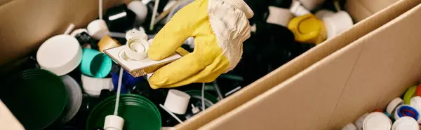 A box overflowing with dirty dishes, as a young volunteer in gloves and a safety vest sorts through the mess. - foto de stock