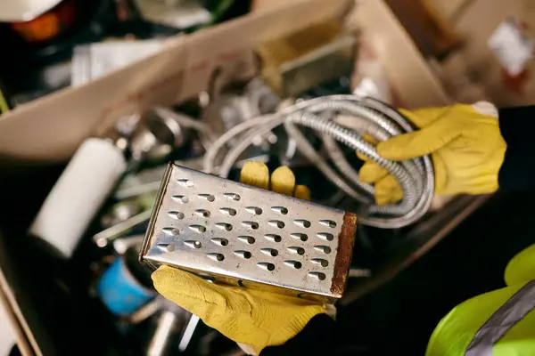 Young volunteer in yellow gloves and safety vest sorting waste with a metal grate in hand. — Stock Photo