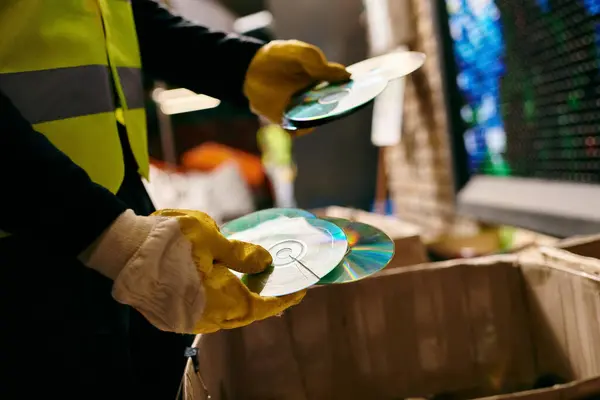 A young volunteer in a yellow safety vest sorts waste, holding cd with eco-conscious intentions. — стоковое фото