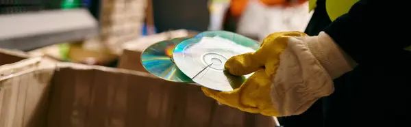 Young volunteer in gloves and safety vest sorting waste, holding compact discs. Eco-conscious action. — Photo de stock