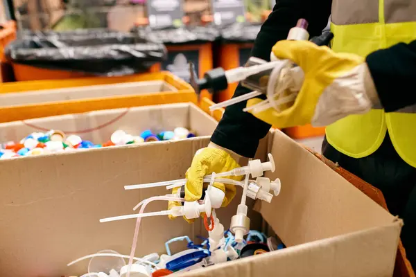 A young volunteer in yellow gloves and safety vest sorts waste, cleaning a box in an eco-conscious effort. — Fotografia de Stock