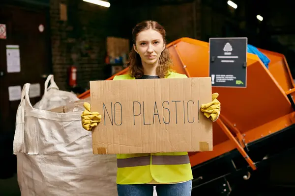 Young eco-conscious volunteer in gloves and safety vest sorting waste, emphatically displaying No Plastic sign. — Stockfoto