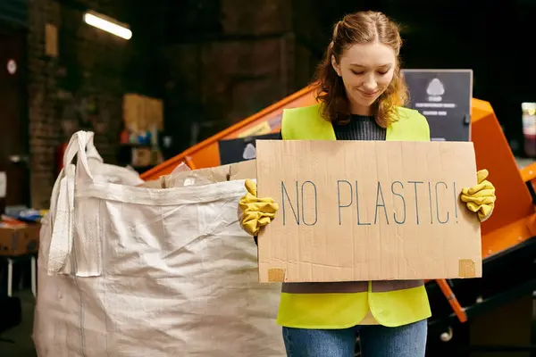 A young volunteer in gloves and safety vest holding a sign that reads no plastic at a waste sorting event. — Stock Photo