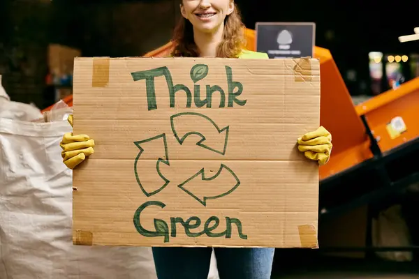 A young volunteer in gloves and safety vest holds a sign that says Think Green while sorting waste, promoting eco-consciousness. — Stockfoto