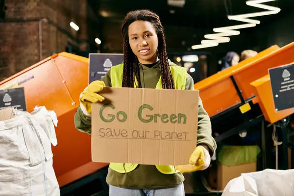 A young woman in gloves and safety vest holds a sign saying go green save our planet in a passionate plea for environmental conservation. — Foto stock