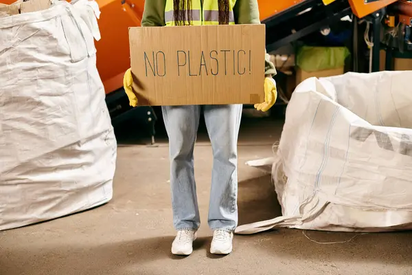 Young volunteer in gloves and safety vest holds sign that says no plastic while sorting waste. — Stock Photo