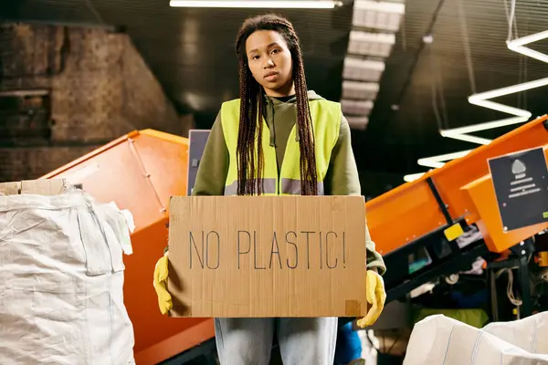 Young volunteer in gloves and safety vest holding a sign that says no plastic while sorting waste. - foto de stock