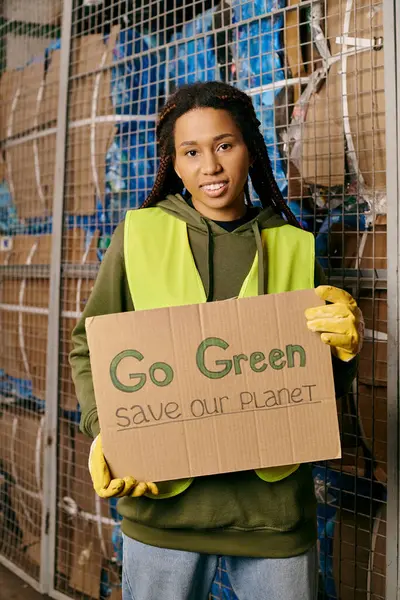 A woman in gloves and safety vest holds a sign urging to go green and save our planet. — Stock Photo