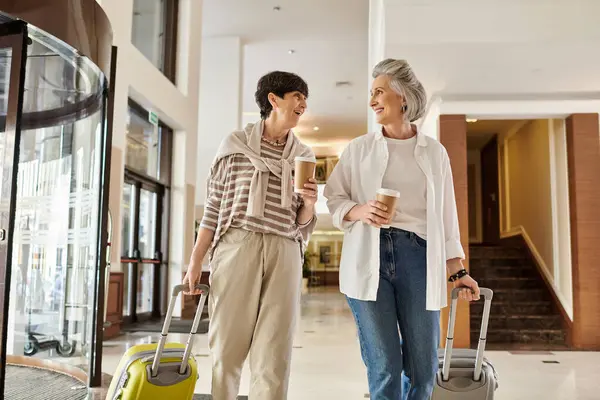 Senior lesbian couple, one holding luggage, the other holding hands, ready for adventure. — Stock Photo